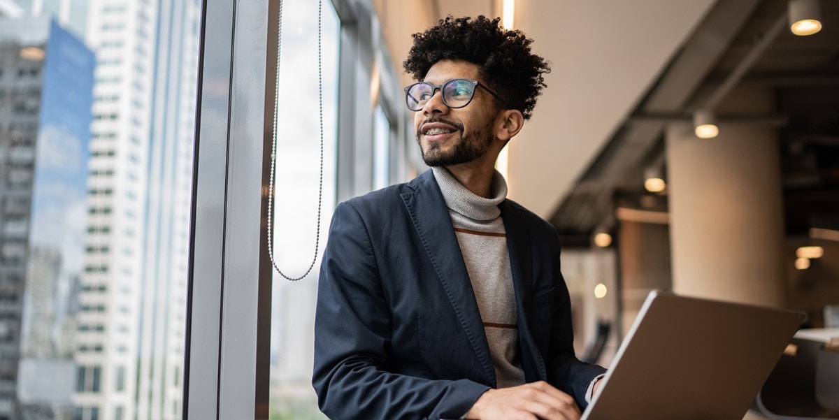 professional man in office with laptop, looking out window in office